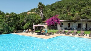 A swimming pool with lounge chairs and a building with a garden in the background.