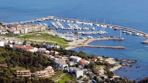 An aerial view of a coastal town with a marina, residential buildings, and a rocky shoreline.