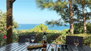 An outdoor dining area with a view of the sea, featuring a table set with wine glasses, a bottle, and a baguette.