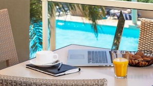 Ein Balkon mit einem Laptop, einer Tasse, einem Glas Orangensaft und einem Korb Kekse, mit Blick auf einen Pool und den Ozean.