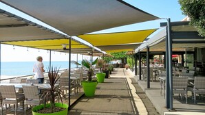 An outdoor dining area with tables and chairs, potted plants, and a view of the sea. - Nice apartment for 6 people with A/C, pool, internet, TV, balcony and pets allowed (Santa-lucia-di-moriani)