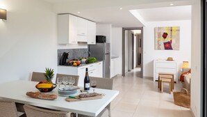 A modern kitchen with white cabinets, a dining area with wicker chairs, and a view into the living room. - Nice apartment for 6 people with A/C, pool, internet, TV, balcony and pets allowed (Santa-lucia-di-moriani)