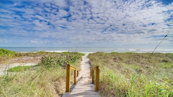 Ein hölzerner Weg führt zum Strand mit freiem Blick auf das Meer und den Himmel.