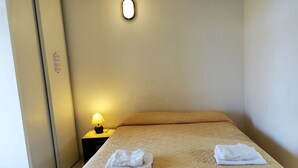 Et hotelværelse med en seng, et natbord med en lampe og en vægmonteret lysarmatur.