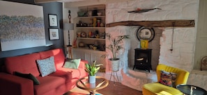 A cozy living room with a red sofa, a yellow armchair, a fireplace, and a bookshelf filled with decorative items.