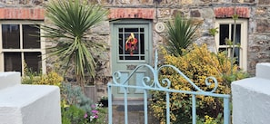 A stone building with a green door, a window with a flower decoration, and a metal gate.