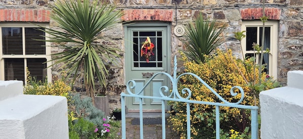 A stone building with a green door, a window with a flower decoration, and a metal gate.
