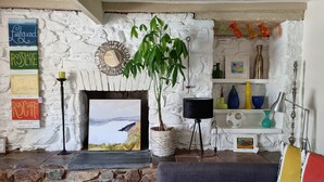 Uma sala de estar aconchegante com lareira de pedra, uma planta verde e uma estante com objetos decorativos.
