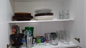 Een keukenkastje met gestapelde borden, kommen en een koffiezetapparaat.