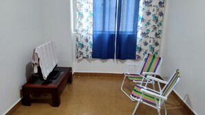 Een kamer met een bank, twee gestreepte stoelen, een raam met blauwe gordijnen en een betegelde vloer.