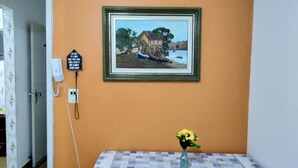 Een kamer met een lijstwerk schilderij van een kusthuis, een telefoon en een vaas met bloemen op een tafel.