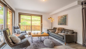 Een moderne woonkamer met een bank, stoelen, een salontafel en een uitzicht door grote schuifdeuren op een terras.