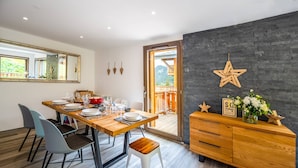 Een moderne eethoek met een houten tafel voor vier personen, een zwarte stenen muur en uitzicht op een houten terras en bergen.