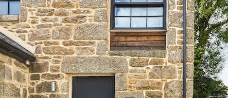 A stone building with a black door and windows, a sign indicating 'Midge 3 The Barn,' and a 'Gratia Guard' sign on a pole.