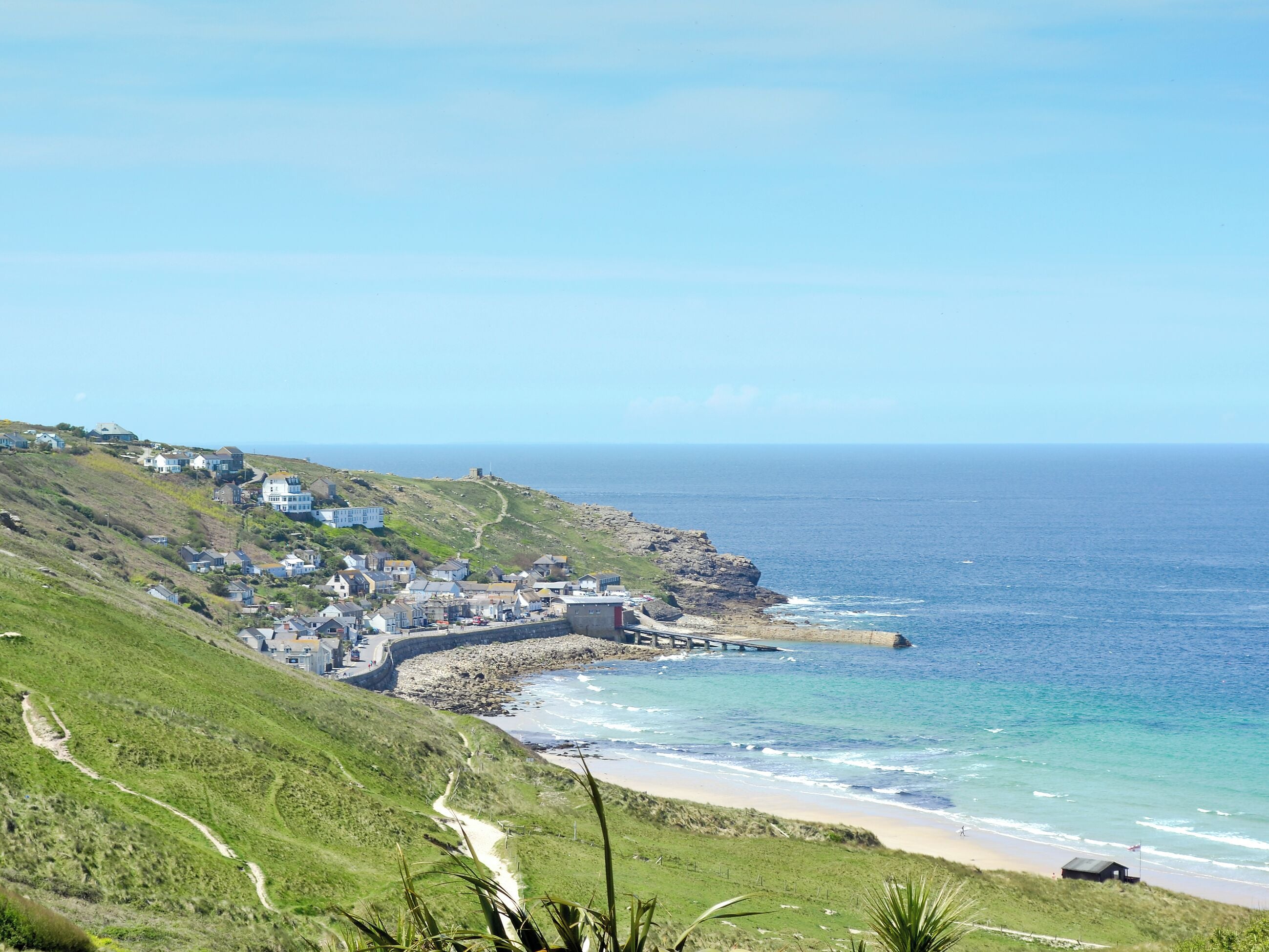 A coastal town with a rocky shoreline, a beach, and a path leading down to the sea.