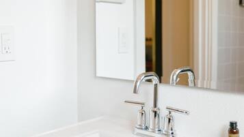 A bathroom with a white sink, two faucets, a mirror, and framed artwork on the wall.