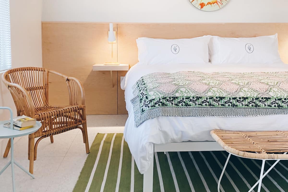 A neatly arranged bedroom with a bed, a chair, a small table, and a wall-mounted lamp.