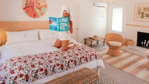 A bedroom with a large bed, a reading chair, a fireplace, and a ceiling fan. - Les Cactus (Palm Springs)