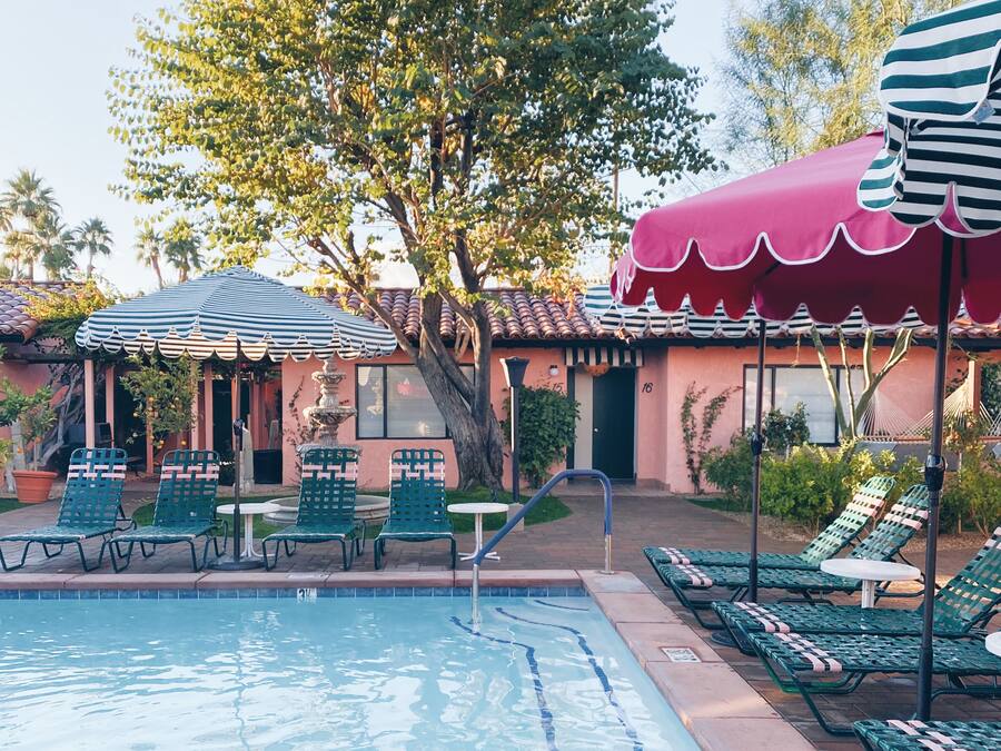 A pool area with lounge chairs and umbrellas, a tiled pool, and a building with a red awning.