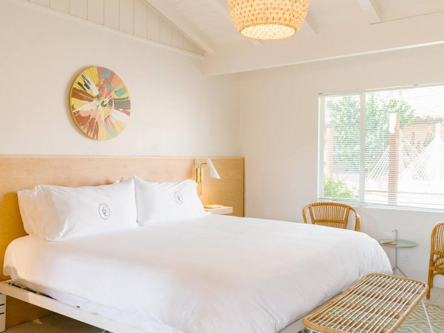 Un dormitorio con cama, lámpara colgante, decoración circular en la pared y ventana con vistas a follaje.