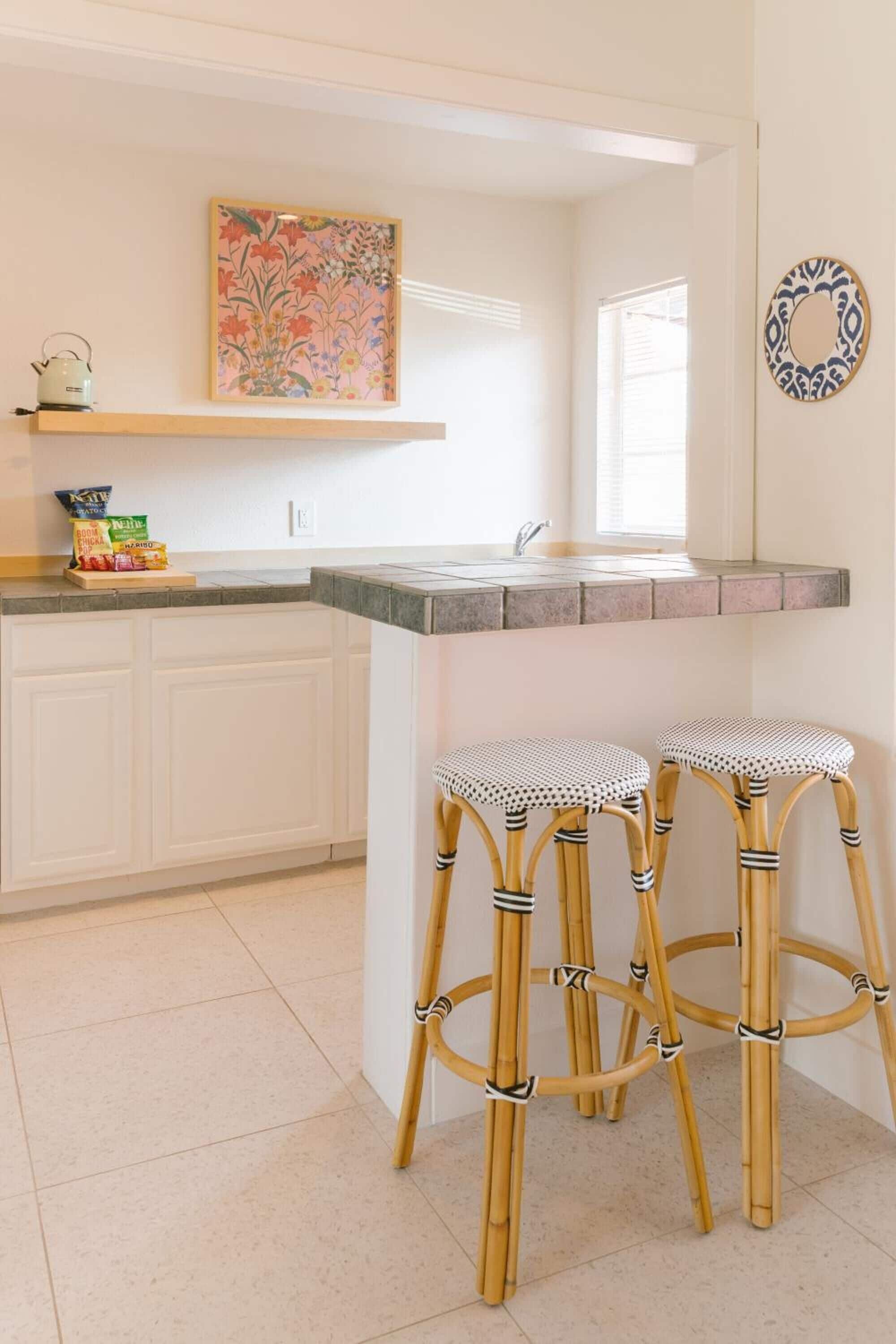 A kitchen with white cabinets, a granite countertop, and two wicker stools.