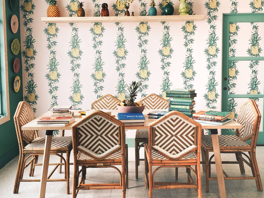 Un coin repas avec une table dressée pour six personnes, entourée de chaises en osier. Une bibliothèque contenant des livres et des objets décoratifs est fixée au mur au-dessus de la table.