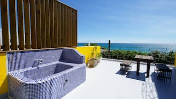 A rooftop terrace with a blue-tiled hot tub, a wooden table and chairs, and a view of the ocean.