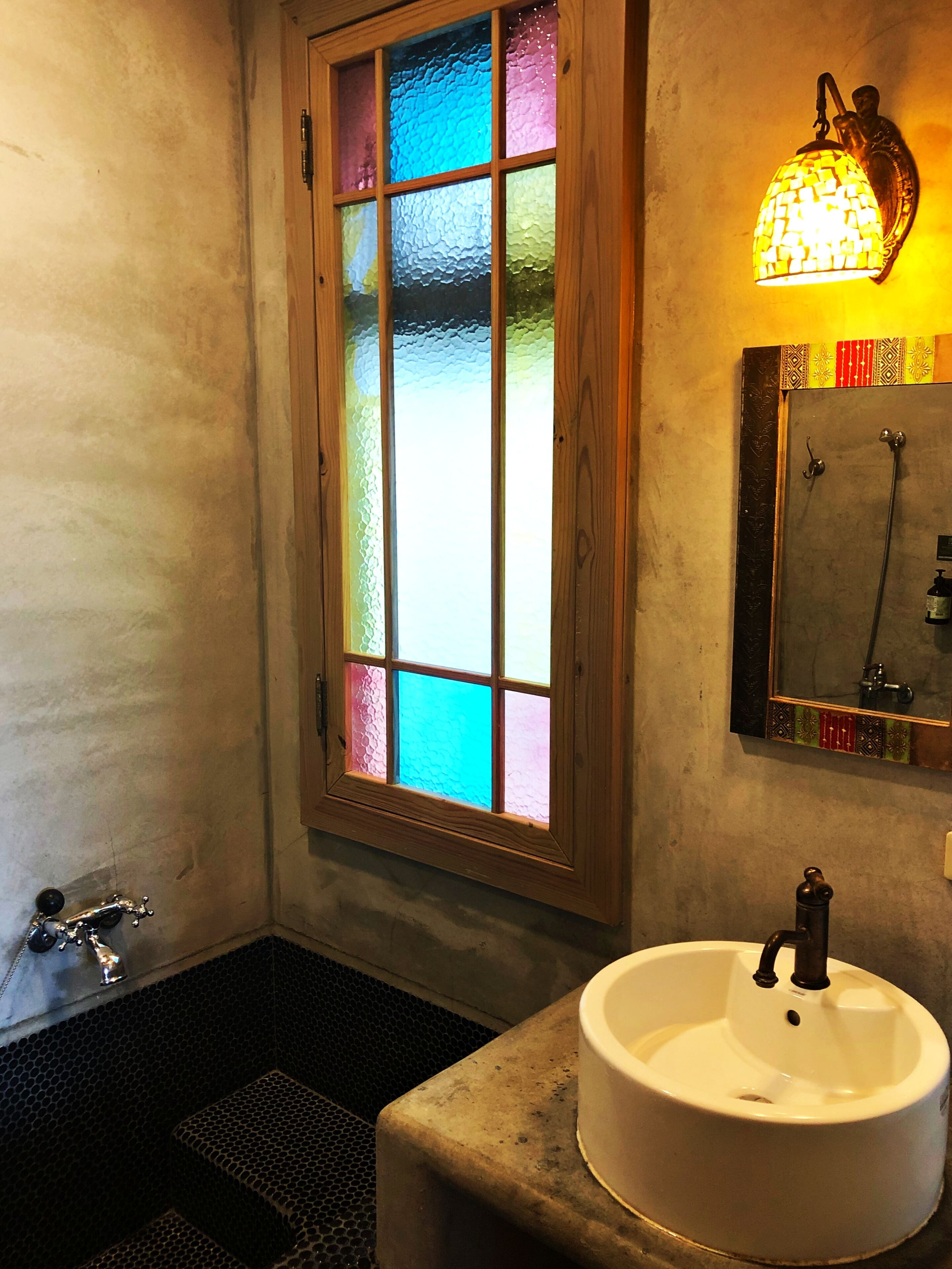 Une salle de bain avec un lavabo blanc, un miroir, une douche et un vitrail.