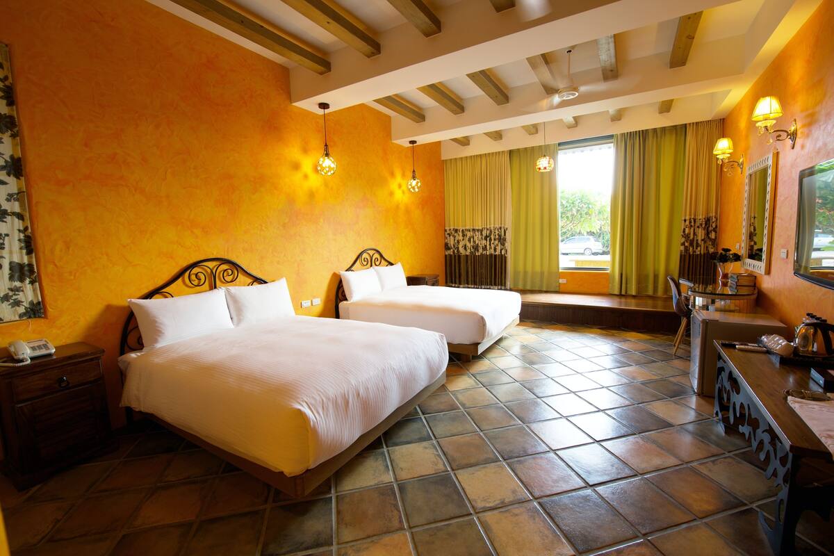A hotel room with two beds, a desk, and a window with curtains.