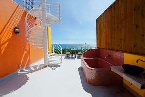 A rooftop terrace with a spiral staircase, a red mosaic bathtub, and a wooden deck with a view of the ocean. - Sand Hostel (Hengchun)