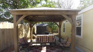 A covered patio area with a table and chairs, a grill, and a wooden fence in the background. -  50% to Book the Gecko Home - Super Clean, Really Nice 3BR - Sleeps 6- By TNT. (Page)
