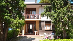 A two-story building with a balcony, a patio area with outdoor seating, and a gravel pathway leading to the entrance. - Nice apartment for 6 people with A/C, TV, terrace and pets allowed (San Michele Al Tagliamento)