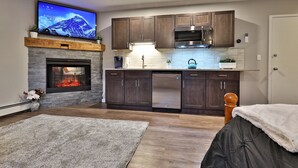 A modern kitchen with dark wooden cabinets, stainless steel appliances, and a flat-screen TV mounted above the fireplace.