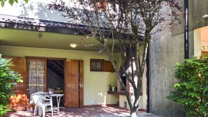 Un patio con una mesa, sillas, una puerta de madera y un árbol pequeño.