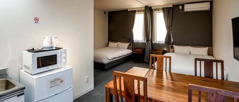 A compact hotel room with a kitchenette, a bed, a sofa, and a dining area.