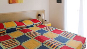 Una cama con un edredón colorido, una mesita de noche con una lámpara y un cuadro en la pared.