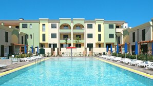 Una piscina con sillas de descanso y sombrillas, rodeada de edificios de varios pisos con balcones.