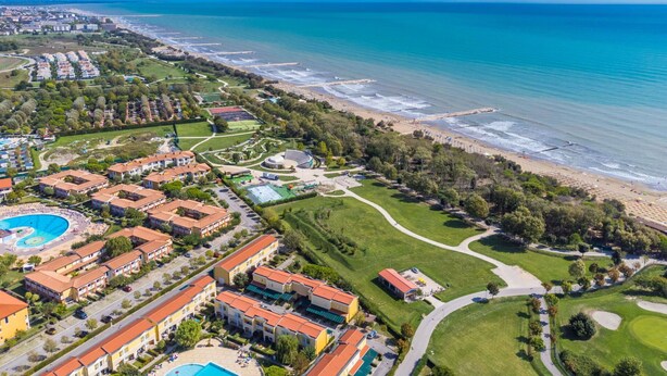 Vista aerea di un resort costiero con una grande piscina, diversi edifici dell'hotel e una spiaggia ben curata.
