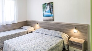 Et hotelværelse med to senge, et maleri af en strandscene og sengeborde med lamper.
