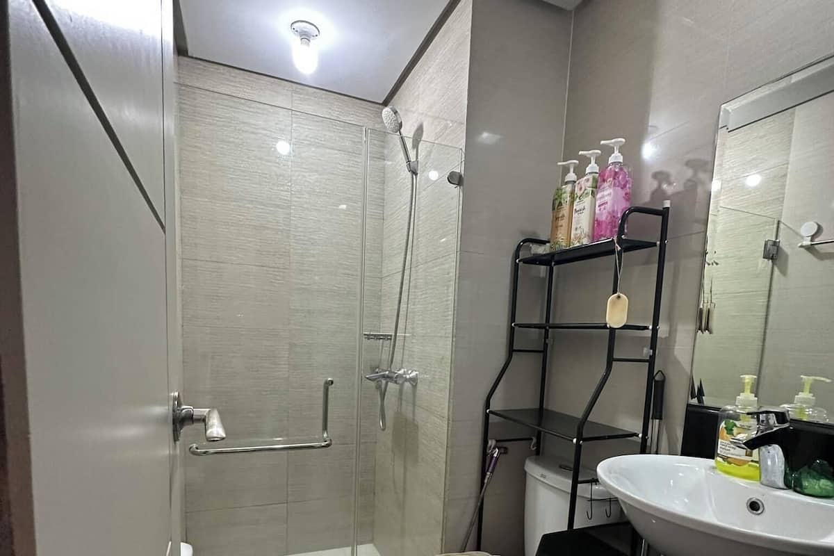 Un baño moderno con ducha envuelta en vidrio, inodoro blanco, lavamanos negro y un espejo.