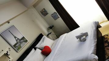 A hotel room with a bed, white linens, a red pillow, a rolled towel, a picture of the Eiffel Tower, and a small plant.