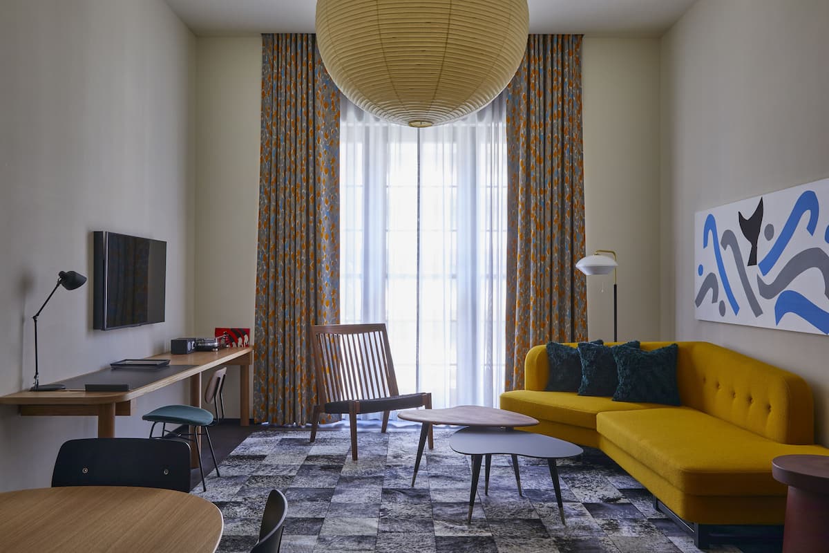 Un salon moderne avec un canapé jaune, une chaise en bois, une petite table ronde et un bureau avec un ordinateur.