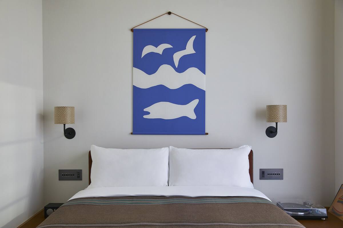 Une chambre d’hôtel avec un lit, deux lampes fixées au mur, une décoration murale bleue et une prise de courant.