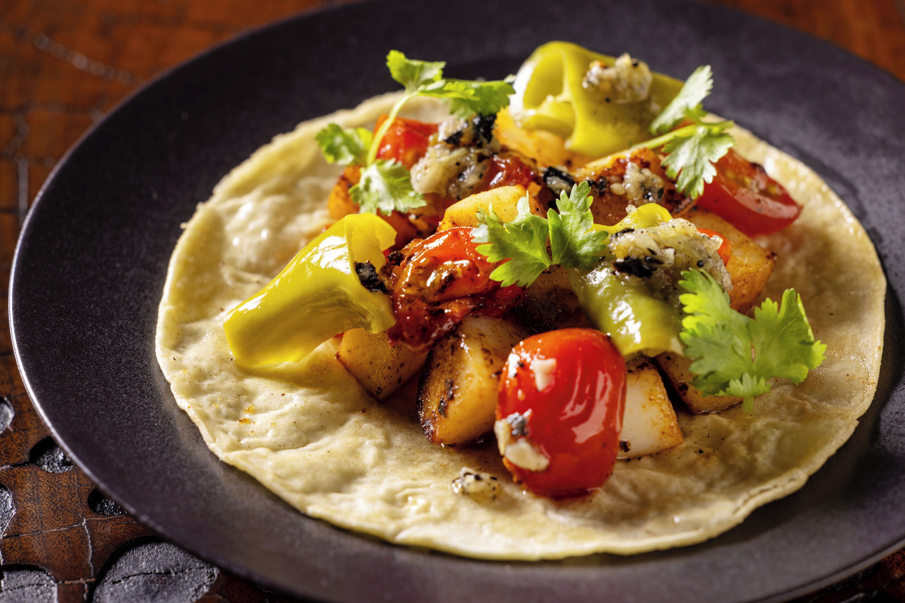 Ein Teller Essen mit Tortilla-Boden, belegt mit gegrilltem Gemüse und Kräutern.