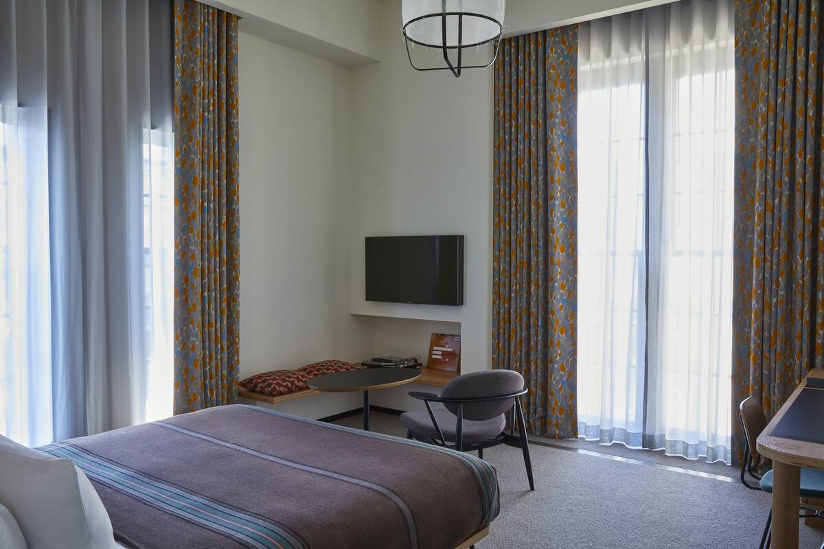 Une chambre d’hôtel avec un lit, un bureau, une chaise, une télévision et des rideaux.
