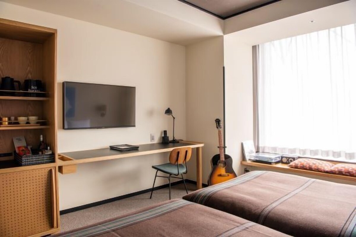 Un dormitorio con cama, escritorio, silla, guitarra y televisor.