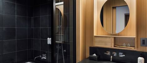 A modern bathroom with a black tiled shower, a white sink, and a wooden vanity.