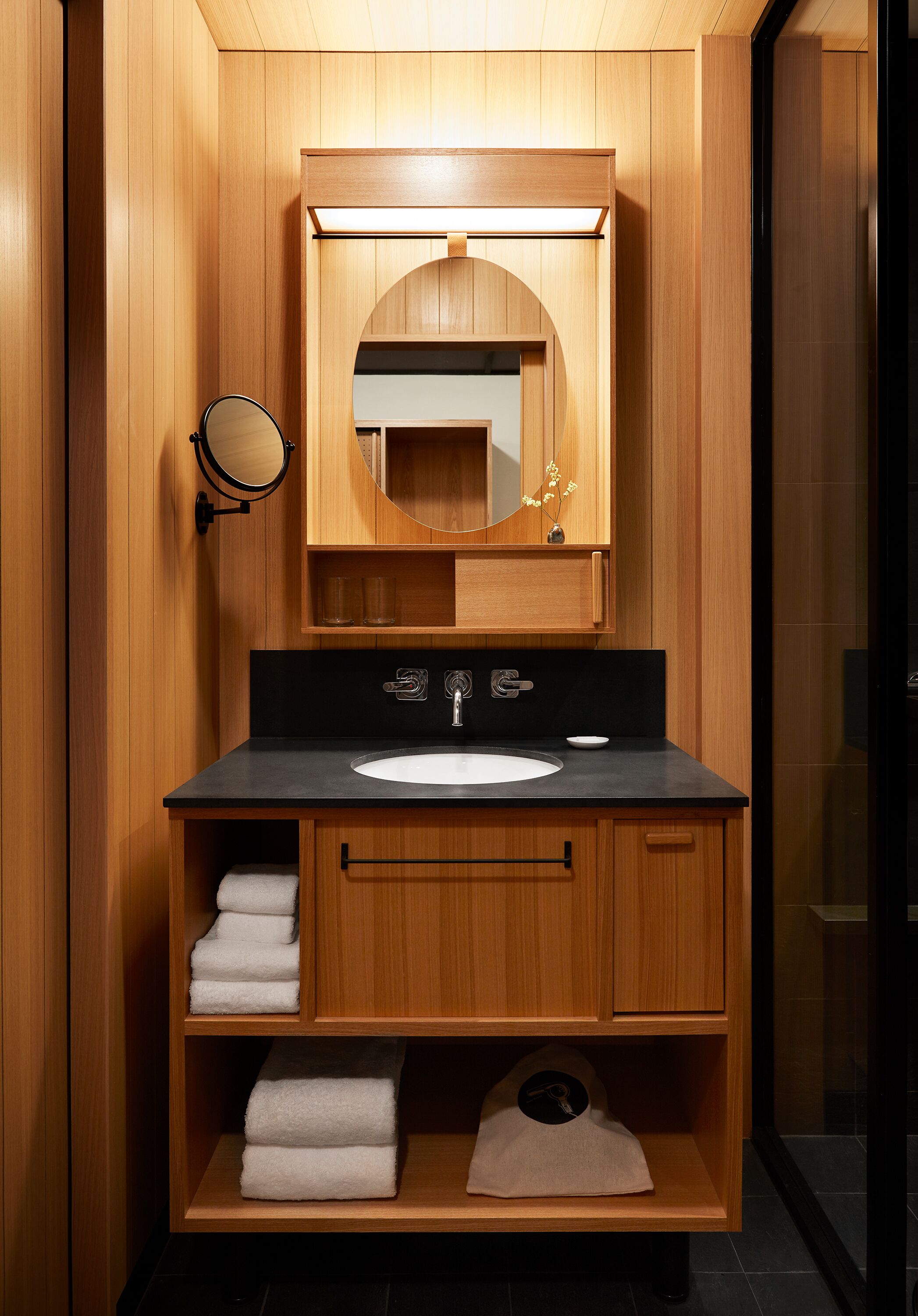 A compact, modern bathroom with a wooden vanity, a mirror, a sink, and a towel rack.