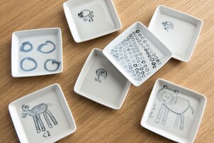 Six square ceramic plates with hand-drawn animal designs, arranged on a wooden surface.