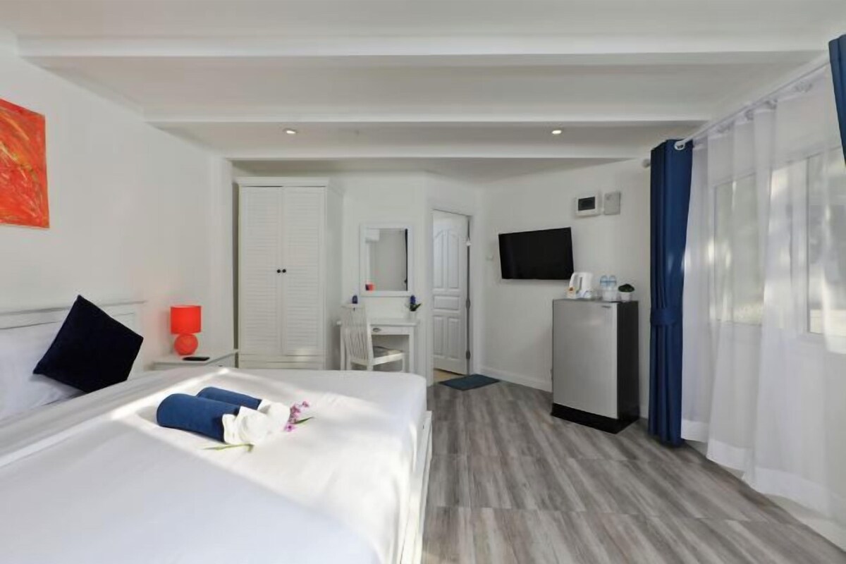 Una habitación de hotel con cama, escritorio, televisor y ventana con cortinas.